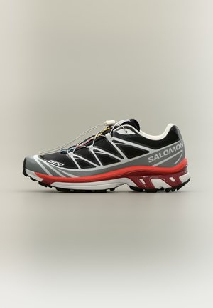 Chaussure de course Salomon noire et grise avec une semelle intermédiaire rouge, des accents blancs et un système de laçage rapide, présentée de profil sur fond neutre.