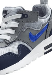 Baskets Nike grises avec des accents bleus, des panneaux en mesh et des lacets blancs. Comprend une languette et un col rembourrés, une semelle texturée et un logo sur la languette.