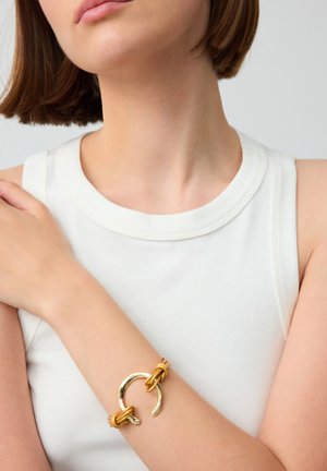 Bracciale dorato con un design in metallo intrecciato, caratterizzato da una finitura liscia e lucida e accenti in pelle annodata di un caldo giallo.