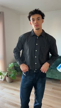 Chemise à rayures noires et blanches avec boutons et manches longues, associée à un jean bleu foncé. Comprend une poche sur la poitrine gauche et des détails à boutons.