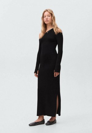 Robe noire à manches longues avec une épaule dénudée, dotée d'une fente sur le côté. Fabriquée dans un tissu lisse, elle présente une silhouette ajustée et un design minimaliste.