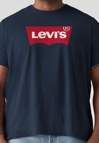 Sötétkék pamut póló, nagy piros Levi's logóval a mellkasán, rövid ujjal és laza szabással. Egyszerű dizájn.