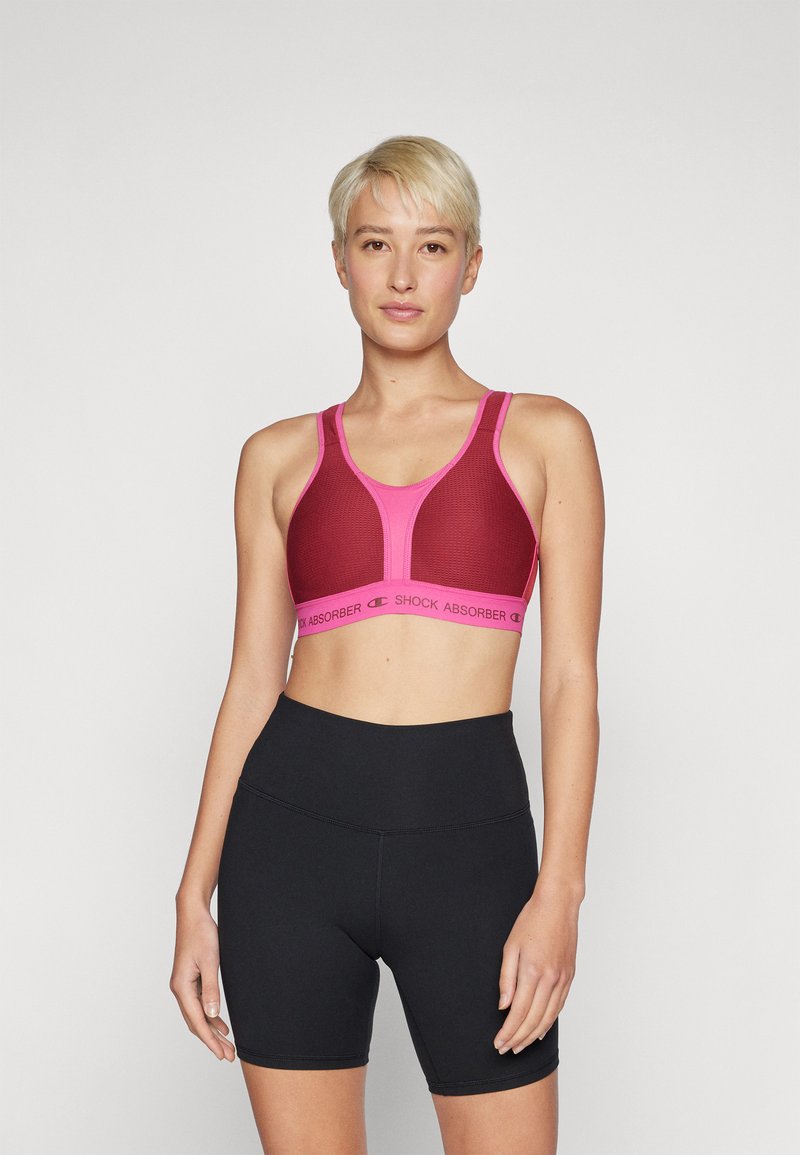 Sostén deportivo rojo con acentos en rosa claro que presenta un diseño de malla y tirantes anchos. Unos pantalones cortos de cintura alta negros completan el look atlético.