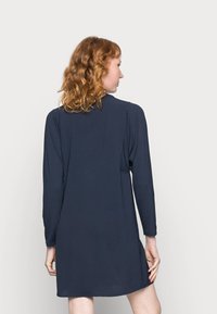 Vestido azul-marinho de mangas longas com um corte descontraído, textura suave e decote arredondado. Apresenta fendas laterais e uma bainha até ao joelho.