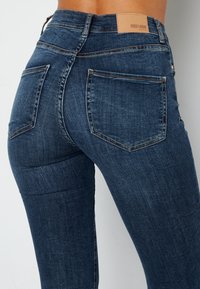 Tmavě modré džíny skinny s vysokým pasem, se koženou nášivkou značky vzadu a dvěma zadními kapsami se švy.