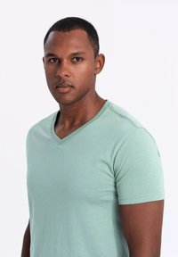 Camiseta de algodón de manga corta en verde menta con escote en V, hecha de una tela suave y que presenta sutilezas en las costuras alrededor del escote y las mangas.