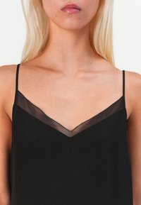 Top senza maniche nero con scollatura a V, bordo trasparente, delicata finitura ondulata e texture del tessuto liscia.