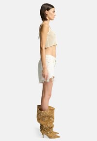 Top court en crochet beige, jupe en denim blanc déchiré, et bottes jaunes à pois avec un bout pointu et un design loose.