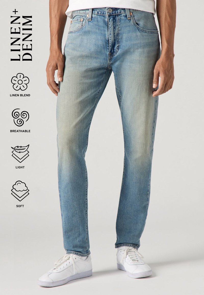 Homme portant un jean en mélange de lin bleu clair et des baskets blanches, avec des icônes mettant en avant les caractéristiques de tissu en mélange de lin, respirant, léger et doux.