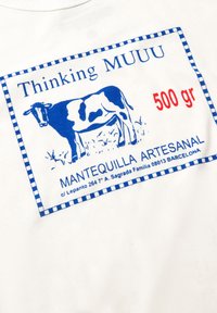 Witte sweatshirt met een blauw en rood grafisch label van een koe, met de tekst "Thinking MUUU" en "MANTEQUILLA ARTESANAL."