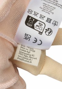 Audinio etiketė šviesiai rožiniame drabužyje, su juodu tekstu pateikiant priežiūros nurodymus ir prekės ženklą, lygios tekstūros.