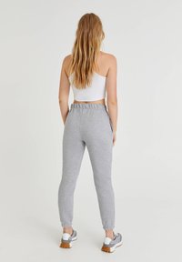 Graue Sweatpants mit tailliertem Schnitt, elastischem Bund und Bündchen. Kombiniert mit einem eng anliegenden weißen Cropped-Top und sportlichen Sneakers.