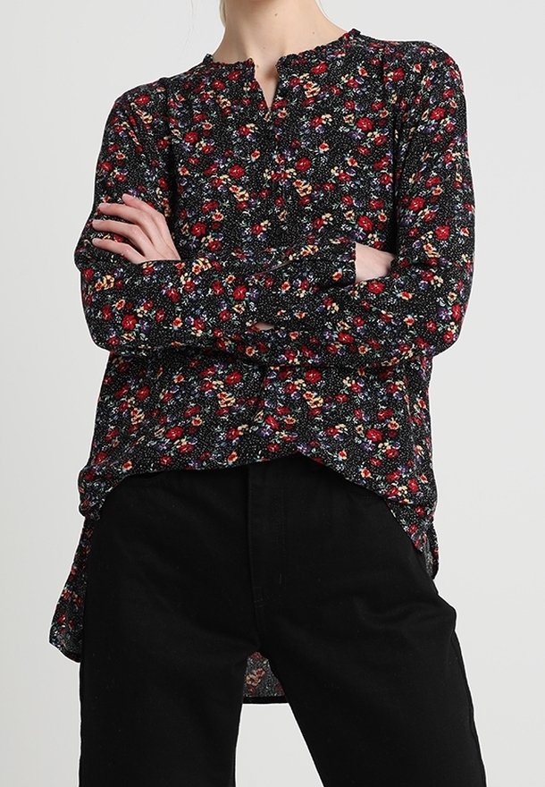 Svart blommig blus med långa ärmar, som har röda och vita blommönster, en rundad halsringning och en något längre baklinje.