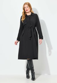Czarny płaszcz trench w pasku, z zapięciem na guziki, długimi rękawami i długością sięgającą do kolan. Noszony z dopasowanymi czarnymi kozakami do kolan.
