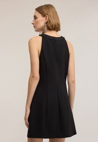 Czarna sukienka bez rękawów z wysokim kołnierzem, zamkiem błyskawicznym z tyłu i rozszerzającym się krojem. Gładka faktura i czyste linie bez dodatkowych wzorów.