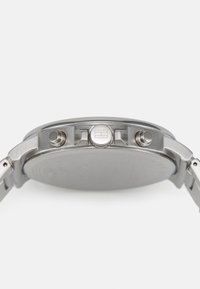 Montre en acier inoxydable argenté avec un boîtier rond lisse, une couronne texturée et deux poussoirs. La finition brossée du bracelet met en valeur l'artisanat.