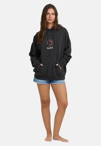 Czarna bluza z kapturem z centralnym wzorem graficznym, w oversize'owym fasonie, z kapturem na sznurki i przednią kieszenią typu kangur. Połączona z dżinsowymi szortami.