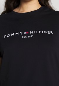 Camisa negra de cuello redondo con el logo bordado de "Tommy Hilfiger" y la bandera, además de "EST. 1985" centrado en el pecho.