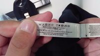 Des mains tiennent une étiquette d'entretien des vêtements montrant les symboles de lavage, les détails du tissu et les informations de recyclage sur un vêtement noir.