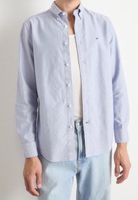 Lichtblauw overhemd met knopen, los gedragen over een wit tanktopje, gecombineerd met lichtblauwe spijkerbroek.