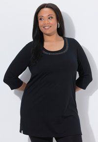 Black tunic with three-quarter sleeves, featuring a scoop neckline adorned with silver studs. Soft, stretchy fabric with side slits.