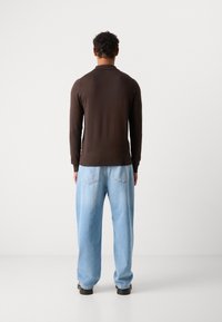 Bruine lange mouw trui met een aansluitend ontwerp, gecombineerd met losse lichtblauwe jeans. Zichtbare naden en twee achterzakken op de jeans.