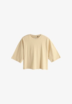 Īsā piedurkņu bēša kokvilnas T-krekls ar brīvu piegriezumu un apaļu kaklu. Gluda tekstūra ar vienkāršu, minimālistisku dizainu.