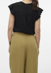 Czarna bluzka z krótkimi falbaniastymi rękawami, z marszczeniem z tyłu, w parze z oliwkowymi spodniami o wysokim stanie i szerokich nogawkach.