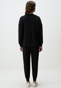 Felpa nera con vestibilità oversize e maniche lunghe, abbinata a pantaloni della tuta tapered in tinta unita; entrambi presentano polsini a coste e una texture morbida.