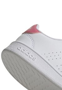 Baskets blanches avec une tige en cuir lisse, accent de talon rose, perforations pour la respirabilité et semelle en caoutchouc texturé embossée du nom de la marque.