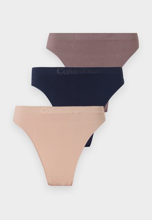 Drie naadloze bikini slips van Calvin Klein in beige, marineblauw en mauve, gestapeld op een lichtgrijze achtergrond.