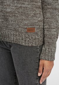 Struktuurne pruun ja hall kudumisest kampsun ribadega lõhiku servaga; esiküljel on nahklabel, millel on "OXMO" logo alumises servas. Stiliseeritud tumehallide teksadega.