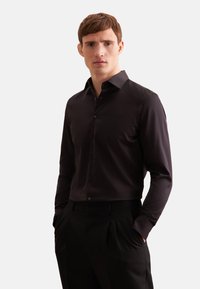 Zwarte langekous met knopen en een spreidkraag, met een gladde textuur en een aansluitend ontwerp, gecombineerd met zwarte op maat gemaakte broeken.