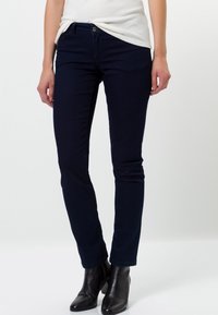 Vaqueros ajustados de color azul marino hechos de denim elástico, con cintura de altura media, bolsillos frontales y un ajuste elegante, combinados con botas negras hasta el tobillo.