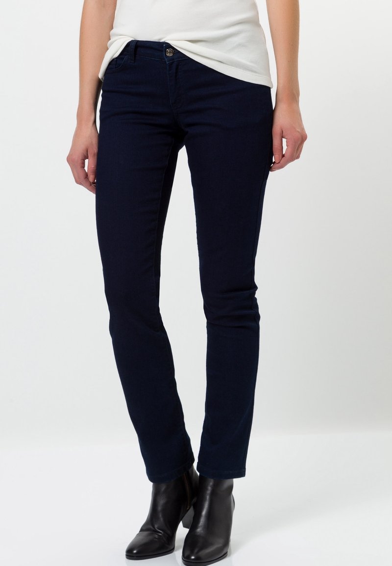 Vaqueros ajustados de color azul marino hechos de denim elástico, con cintura de altura media, bolsillos frontales y un ajuste elegante, combinados con botas negras hasta el tobillo.