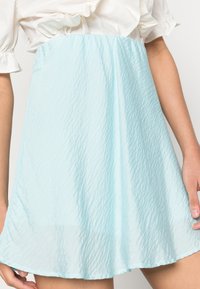 Saia azul clara amassada, feita de um tecido leve e translúcido, com um design fluido, bainha arredondada e textura subtil.
