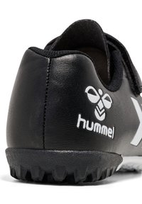 Talons de chaussures de sport Hummel noirs avec semelle texturée et logo blanc sur le côté, présentés sur fond blanc.