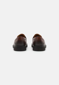 Zapatos de cuero marrón con un acabado suave, forma redondeada, suelas de goma negra y un detalle de costura minimal en el talón.