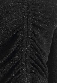 Svart tyg med en mjuk, texturerad yta som har en rynkad detalj som löper vertikalt. Subtila glittrande accenter förbättrar det övergripande utseendet.