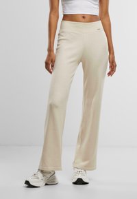 Pantaloni beige a gamba larga con una texture a coste, vita alta e una piccola etichetta del marchio sul davanti. Abbinate a sneakers bianche.