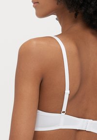 Biały biustonosz z regulowanymi ramiączkami, gładką strukturą i zapięciem na haftkę z tyłu. Prosty design bez widocznych zdobień.