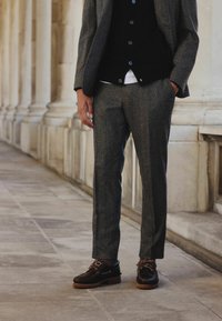 Gray tweed suit with a slim fit, paired with a black button-up shirt. Brown leather shoes with laces and textured soles.
