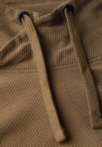 Hnědá strukturovaná tkanina s vzorem včelí plástve a silnými šňůrkami. Obsahuje kovové očky pro funkčnost a vyztužení.