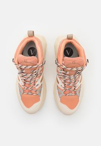 Peach and beige sneakers with a textured fabric upper, reflective accents, and patterned laces. Chunky sole and pull tab on the heel.