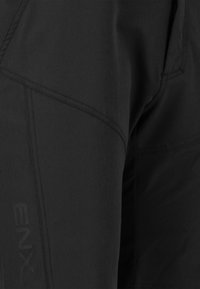 Schwarze Oberbekleidung mit einer glatten Textur, kantigen Nahtdetails und einem schwachen Logoakzent auf dem Stoff.