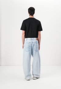 Schwarzes Baumwoll-T-Shirt und blaue weite Denim-Jeans mit einem hellen Waschung, ausgestattet mit Gesäßtaschen und einem Bund mit einem Logoschild.