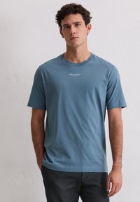 Jasnoniebieska bawełniana koszulka z krótkimi rękawami, okrągłym dekoltem i białym logo nadrukowanym na piersi. Gładka faktura i swobodny krój.