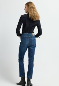 Jeans de color azul oscuro con corte recto, cintura alta y dos bolsillos traseros. Combinados con una camisa negra de botones y botas de tobillo.