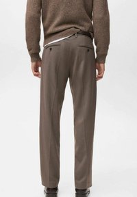 Suéter marrón texturizado sobre pantalones claros, que cuentan con un acabado suave, lazos para cinturón y dos bolsillos traseros. Corte entallado con un diseño de pierna recta.