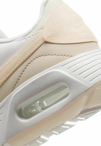 Baskets avec une tige en cuir beige et blanc, des accents texturés, une unité d'amorti visible dans la semelle, et une semelle extérieure en caoutchouc rainurée.